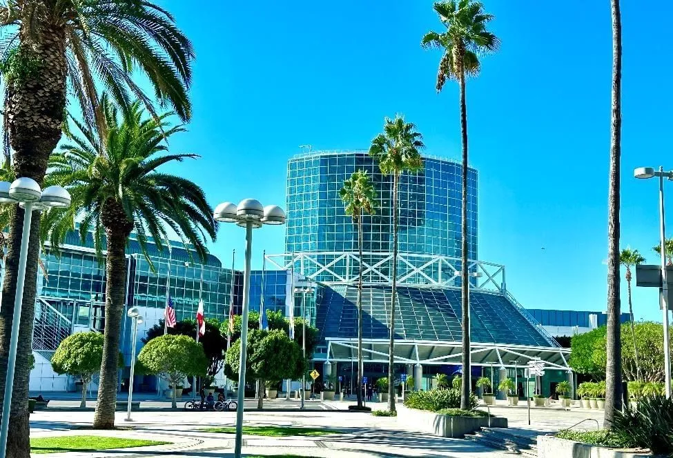 A large glass building with a unique curved design, surrounded by palm trees and street lights.