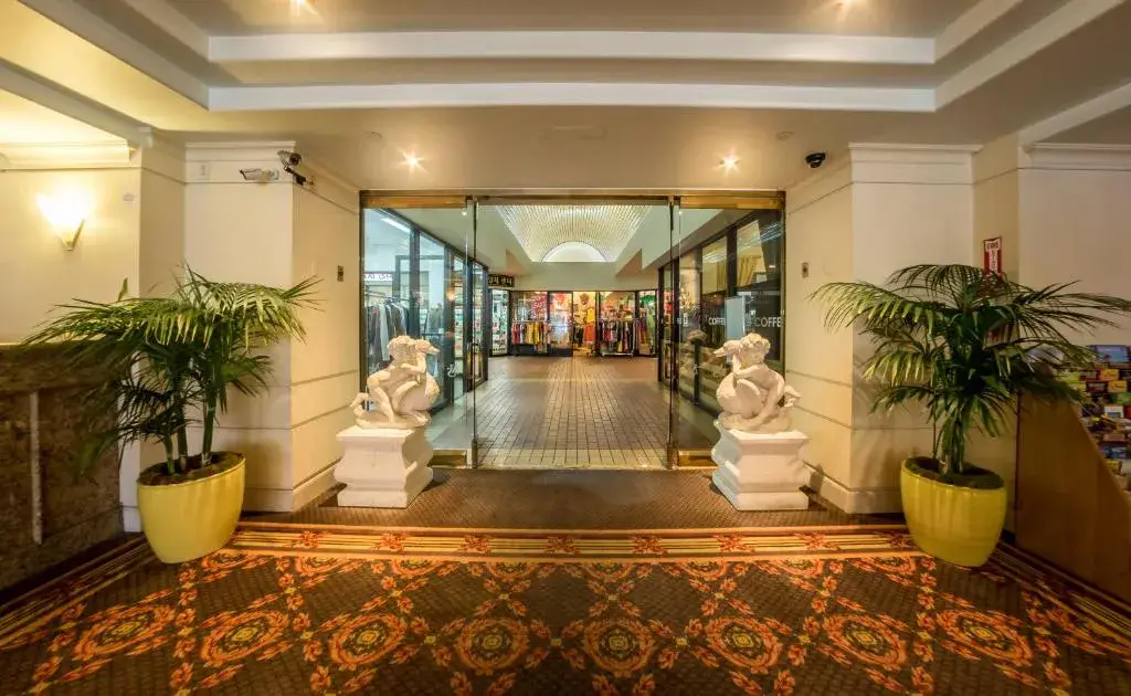 A lobby with a glass door, two potted plants, and two statues